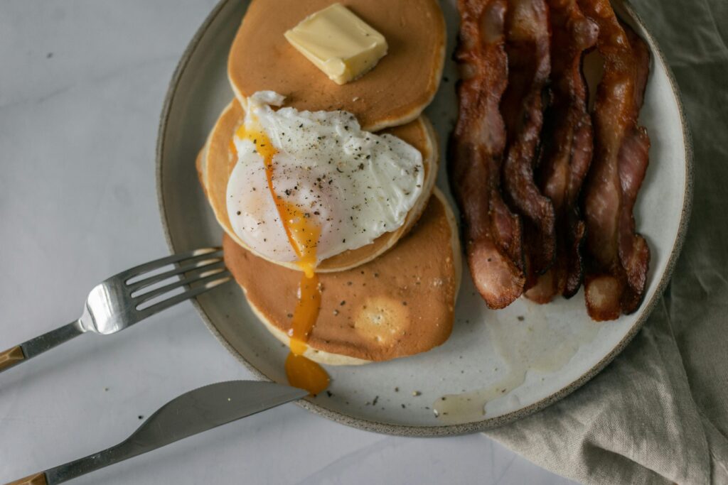 A delectable breakfast featuring pancakes, poached egg, and crispy bacon on a plate.